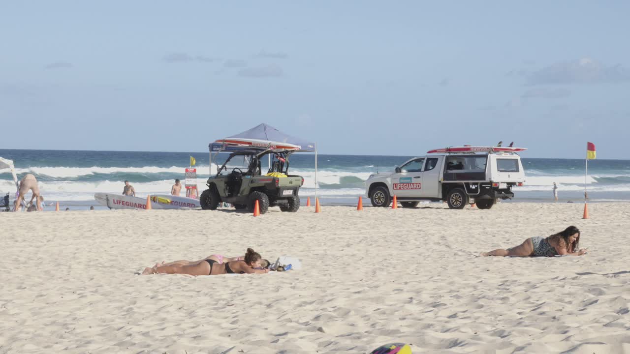 Australian beach with tourists sunbathing, lifeguard transport parked on the sandy beach.