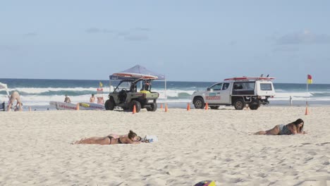 australian beach with tourists sunbathing, lifeguard transport parked on the sandy beach.