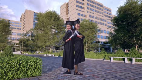 cuerpo lleno de estudiantes asiáticas graduadas con gorras y túnicas cruzando los brazos y sonriendo a la cámara frente a un magnífico edificio universitario