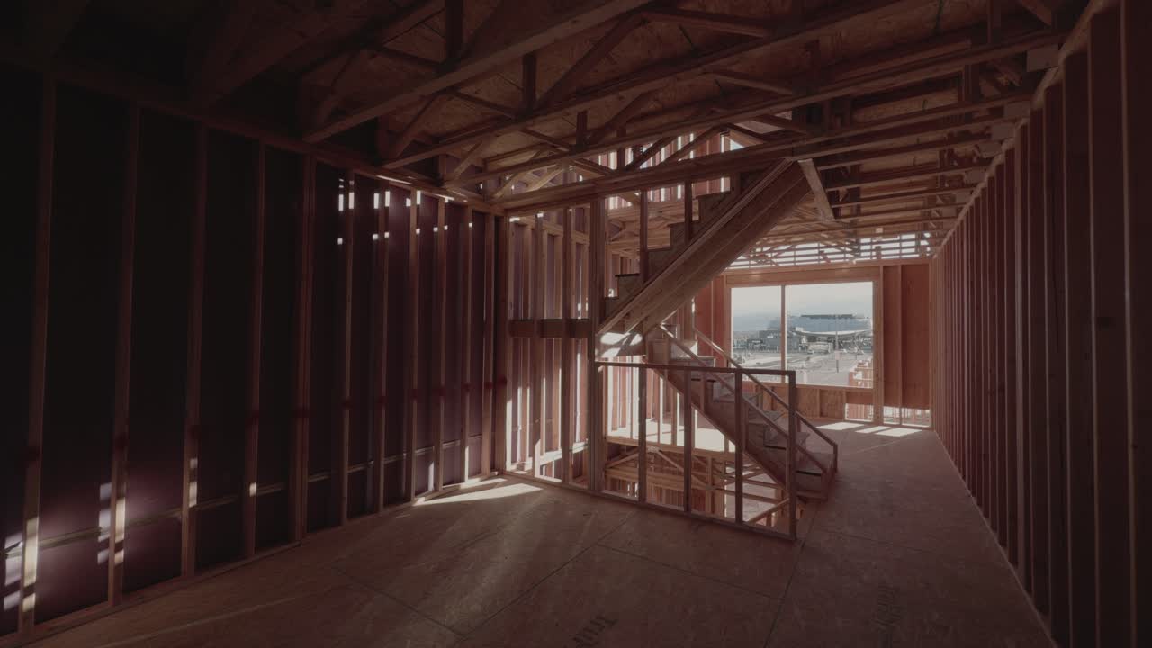 Wide interior view of unfinished wooden house framing with staircase and soft pan