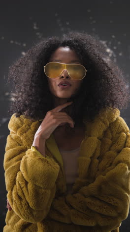 vertical video: stylish woman in yellow fur coat adjusting sunglasses, embracing grunge fashion