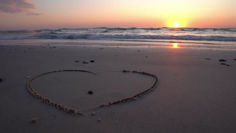 símbolo de corazón dibujado en la arena contra un telón de fondo de puesta de sol sobre el mar