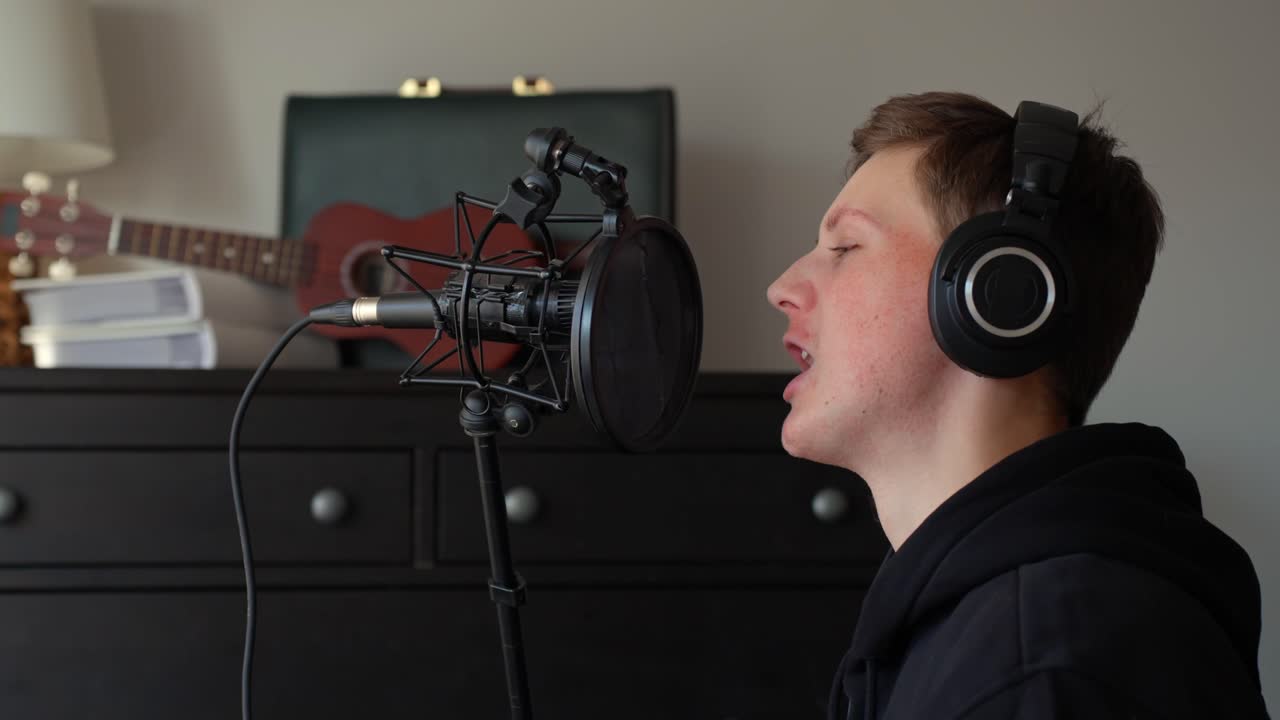 Young man recording vocals in home music studio, passionately singing into a professional microphone and wearing headphones, creating new song for his album