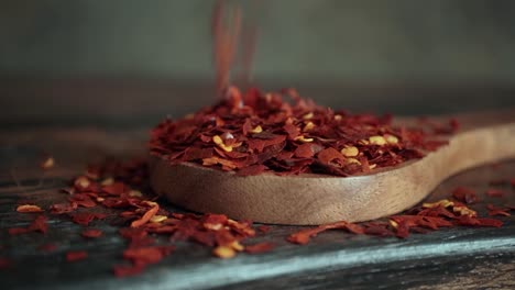 flakes of red hot chili pepper in wooden spoon closeup on a kitchen table.