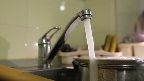 a sink full of dishes while water from the tap pours over the dishes, close up