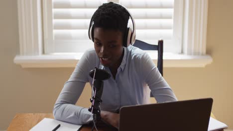 African-american-woman-wearing-headphones-talking-in-microphone-while-looking-at-laptop