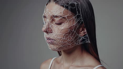 serene fashion model wearing intricate white mesh mask, standing with closed eyes against neutral gray background, embodying contemporary elegance and artistic design