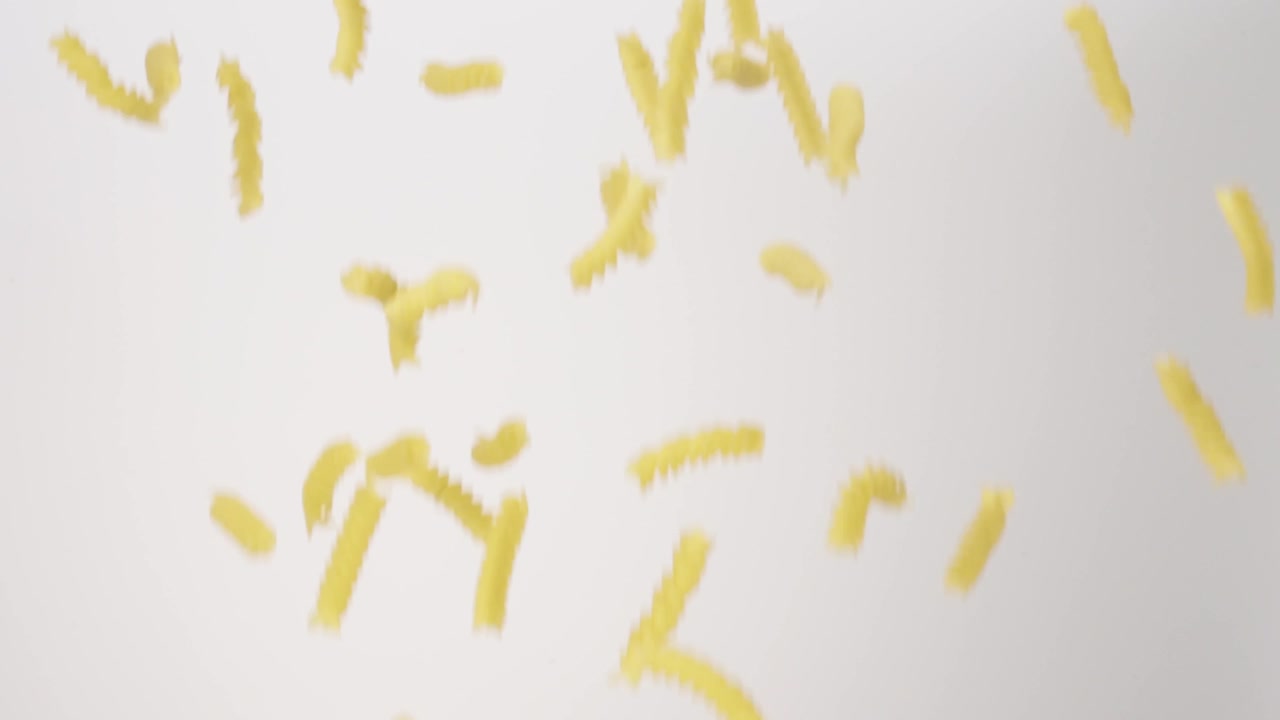 Dry uncooked Fusilli Rotini raining down on a white backdrop in slow motion close up macro.