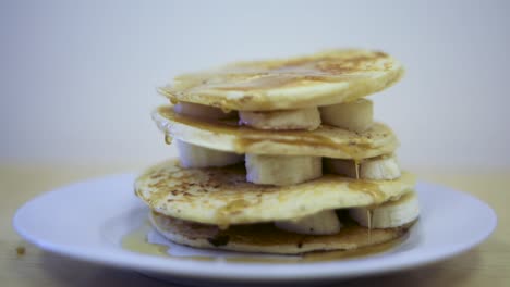 delicious breakfast of stacked banana pancakes with syrup dripping down the layers, close-up