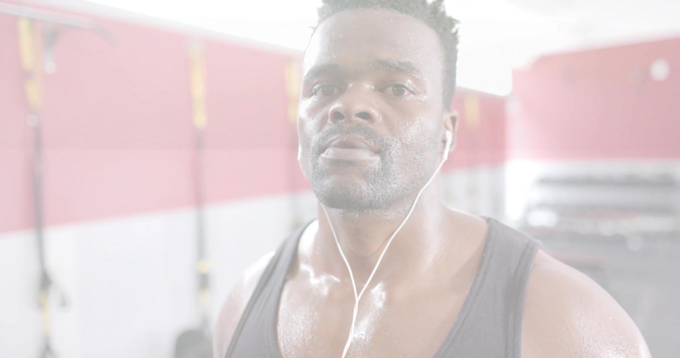 Video verticale: Uomo in palestra che si ferma per recuperare mentre ascolta gli auricolari, con un'inquadratura che rivela il TRX.