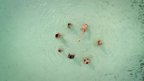 vista aérea de un grupo de amigos en trajes de baño jugando al voleibol en el mar cerca de la playa.