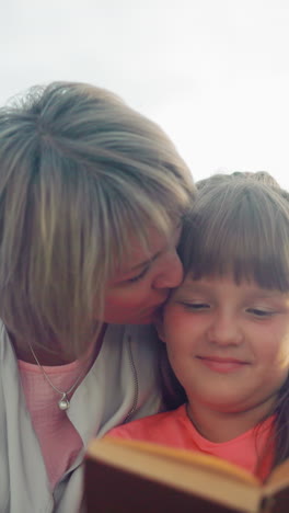 madre abraza cálidamente a su hija en rosa mientras leen un libro juntos, con una suave sonrisa en el rostro del niño y el sol brillando por detrás