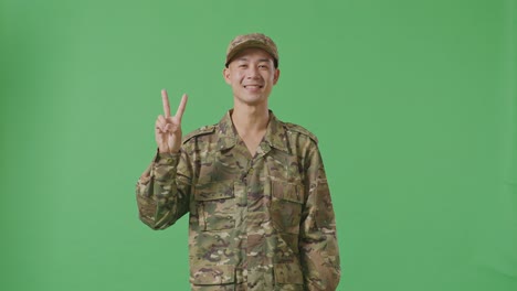 asian man soldier smiling and showing peace gesture to camera while standing in the green screen background studio