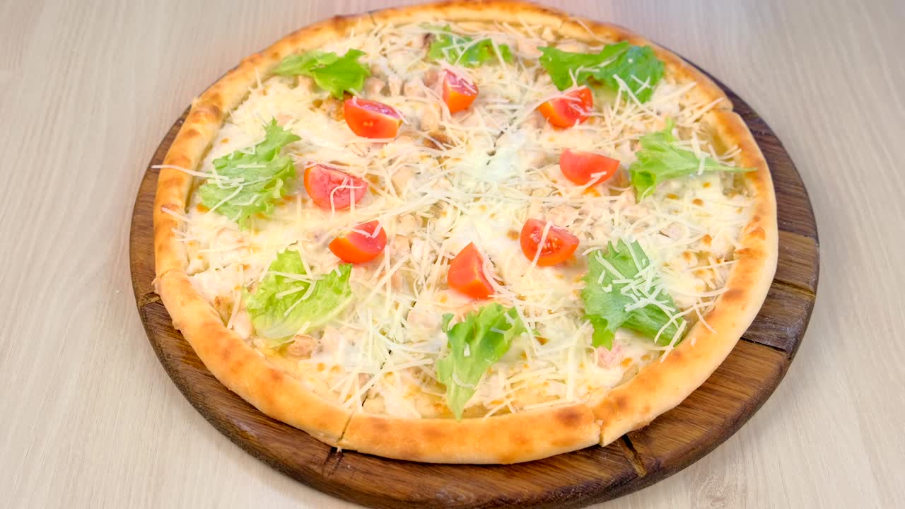 Pizza with chicken and cheese, tomatoes and lettuce on top on wooden board.