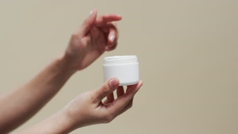 de manos de mujer sosteniendo crema en fondo beige con espacio de copia, cámara lenta
