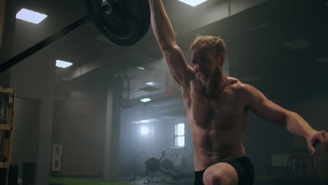 the boy pushes the barbell in the gym with one hand. an athlete without a t-shirt in a dark room lifts the barbell while practicing the force of the impact