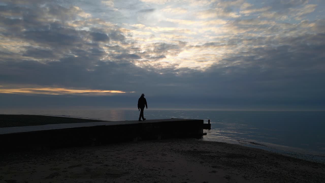 silueta en cámara lenta de un hombre caminando hacia el final de un muelle al atardecer en la playa de fleetwood, lancashire, reino unido