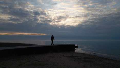 slow motion silhouette of man walking to the end of a jetty at sunset on fleetwood beach lancashire uk