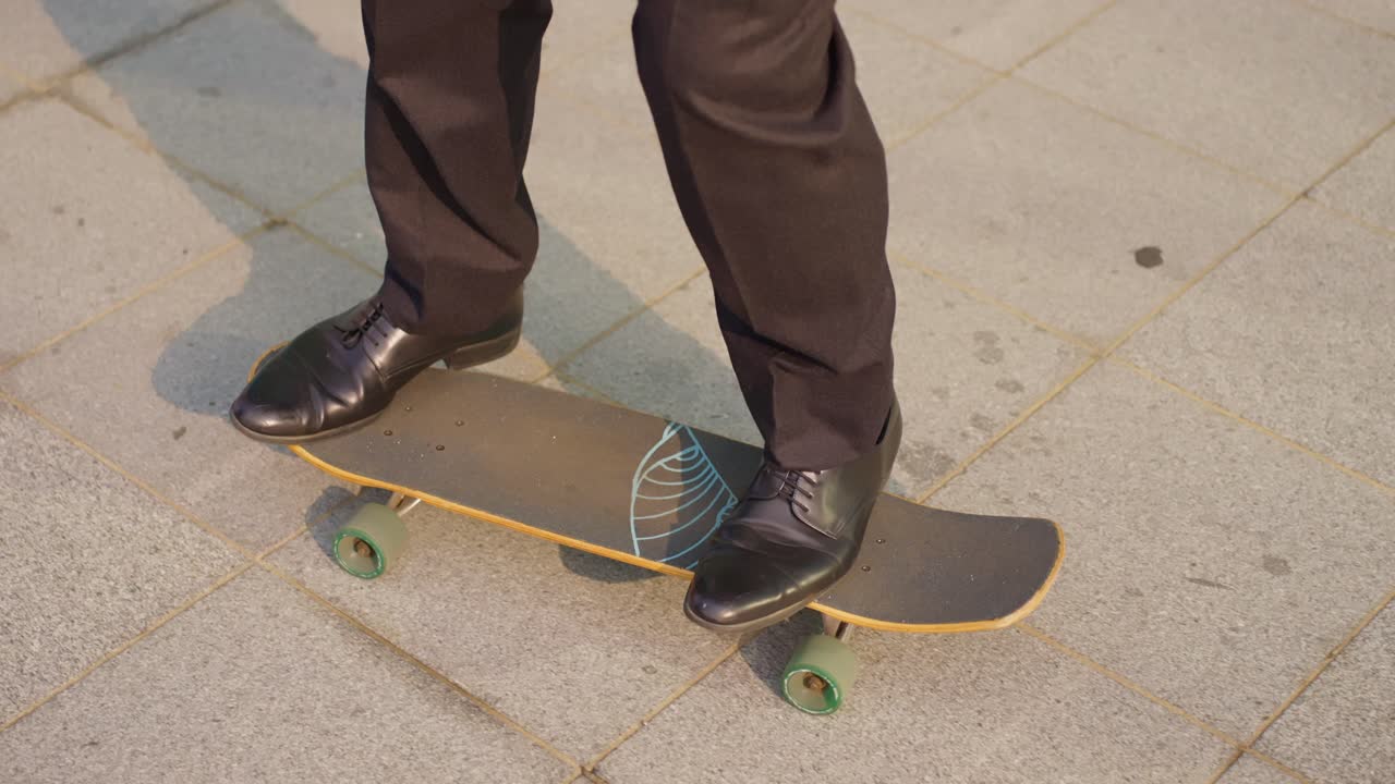Close-up tracking shot of businessman legs in suit pants and dress shoes performing skateboarding tricks on skateboard with green wheels on paved city plaza in Seoul slow motion