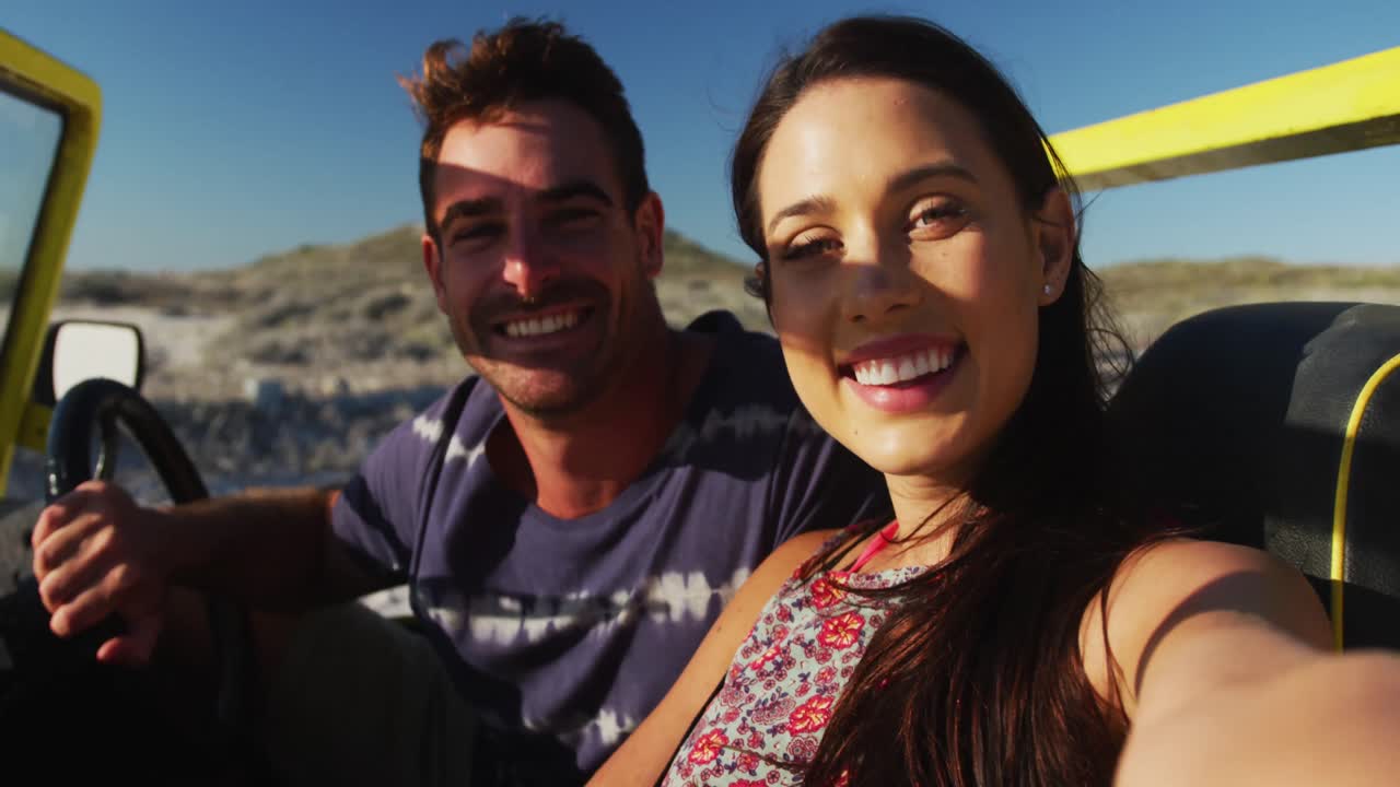 Šťastný pár sedící v plážovém buggy u moře používá chytrý telefon a pořizuje si selfie.