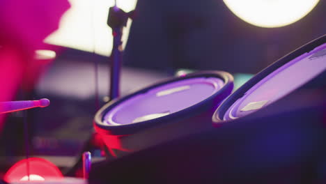 close up of drum pads under colorful studio lighting with soft blur in background and visible stand, showing percussion instrument in performance or practice environment with artistic color gradients