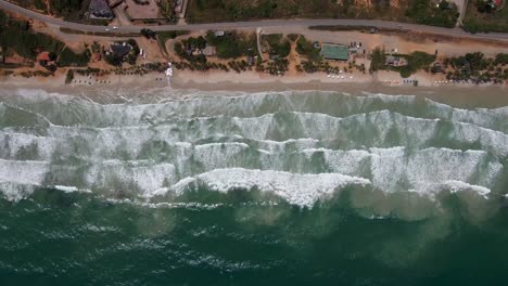 El-Dron-Se-Desliza-Hacia-La-Izquierda-Y-Revela-Una-Playa-Con-Complejos-Turísticos,-Automóviles,-Sombrillas-Y-Gente-Disfrutando-Del-Agua,-Porlamar,-Isla-Margarita,-Venezuela.