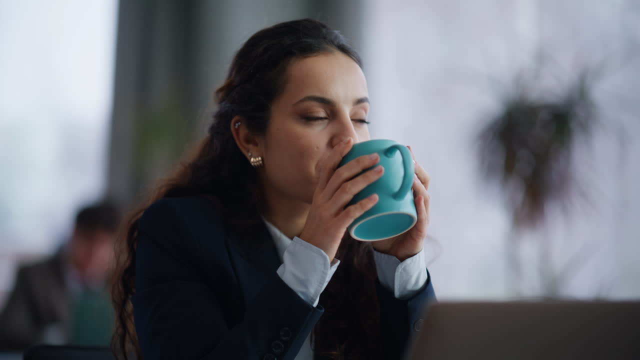 Drømmende forretningskvinde holder kaffekop i et coworking-område tæt på. Dame holder pause
