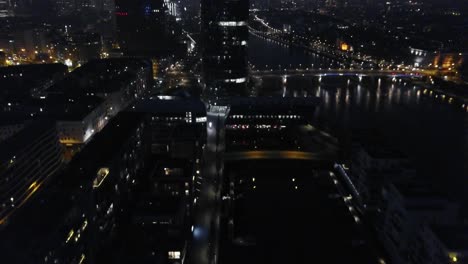 flying backwards with buildings next to the river main in frankfurt at night
