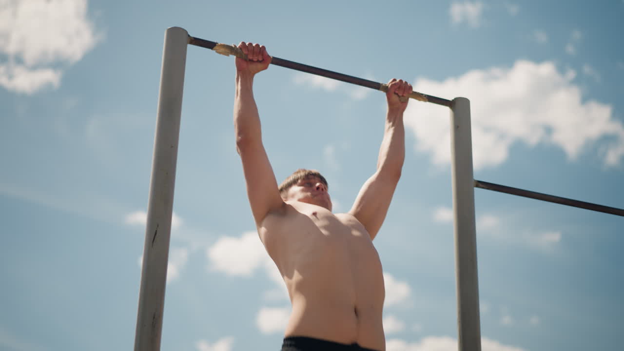 야외에서 운동을 추구하는 모습이에요. 용감한 소방관 후보생이 밖에서 턱걸이 연습을 하고 있어요. 헌신적인 소방관 견습생이 탁 트인 공원 구역에서 밝은 햇빛 아래 절도 있는 턱걸이를 하고 있습니다.