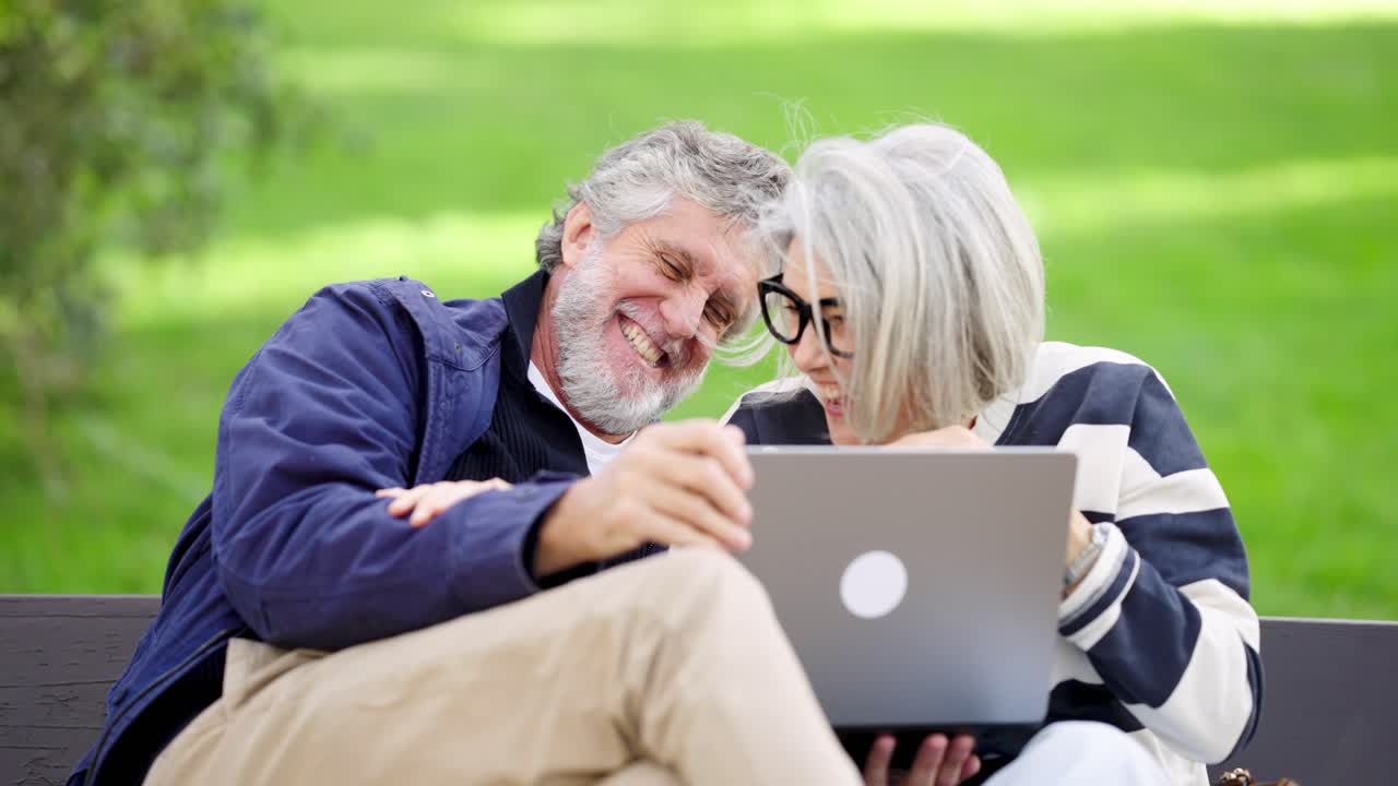 Pareja de ancianos feliz riendo con un portátil en el parque