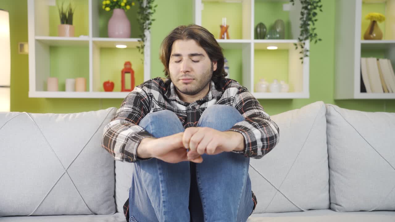 un joven deprimido y preocupado sentado solo en el sofá de su casa.
