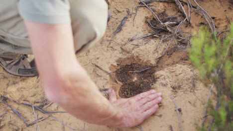 Caucasian-male-survivalist-in-wilderness-examining-and-measuring-animal-print-in-sand-with-hand