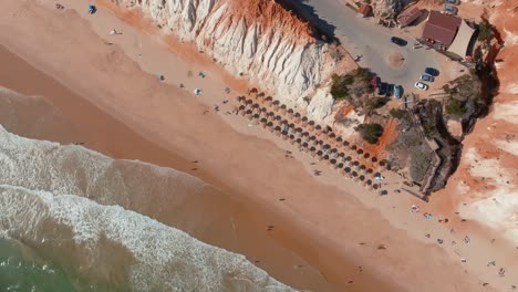 Red-white-rock-and-golden-sandy-beach-with-umbrellas-in-perfect-rows,-drone-aerial-view