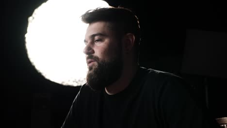 Male with beard talk during podcast, black studio background and bright light
