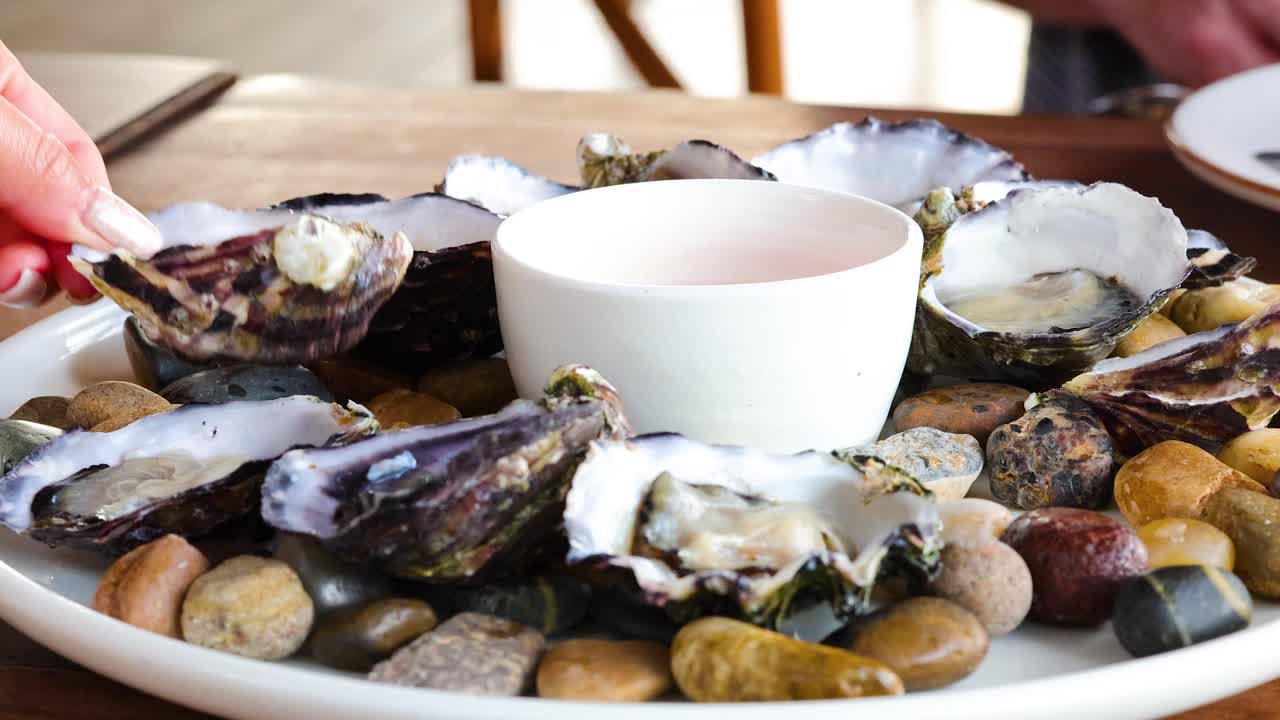 A gourmet oyster platter is prepared with sauce on a wooden table, highlighting fresh seafood and culinary presentation