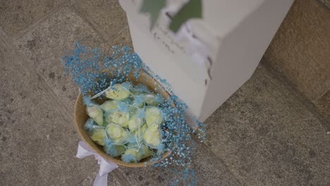 basket of white roses and blue baby's breath beside a white box on a stone floor, suggesting wedding decor