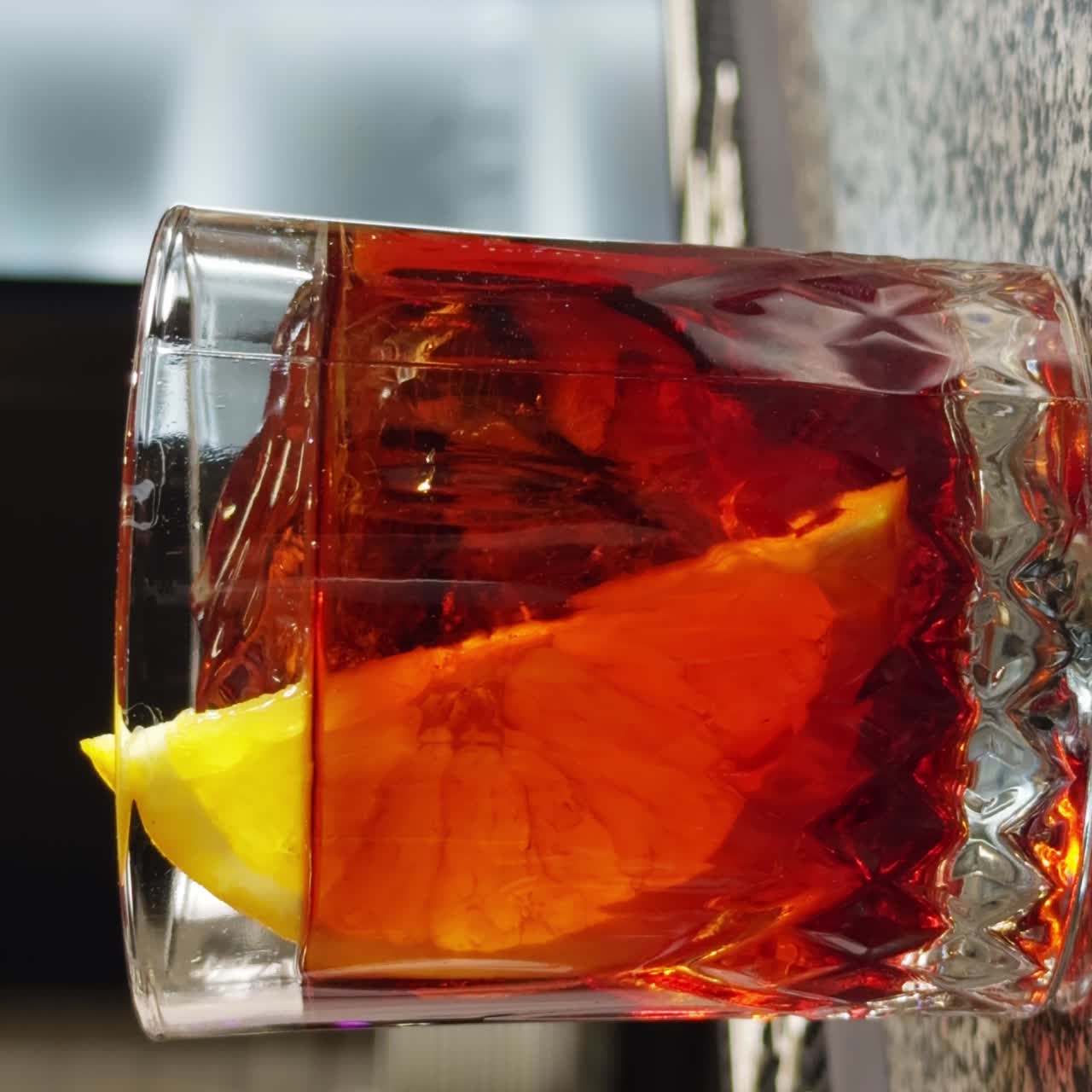 Bevanda all'arancia con cubetto di ghiaccio in un bicchiere old-fashioned. Una fetta di limone viene messa nella bevanda con le pinze. Primo piano. Sfondo sfocato