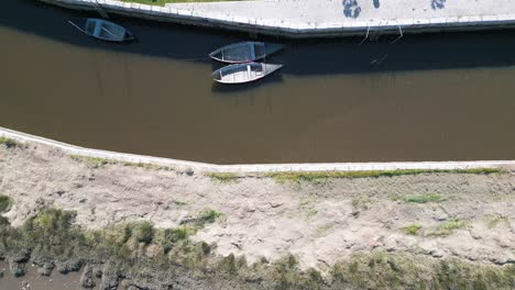 Small-boats-resting-on-the-serene-tributary-of-Ria-de-Aveiro,-reflecting-Portugal's-tranquil-coastal-charm---aerial