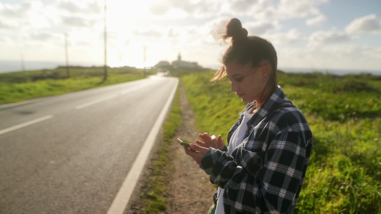 mujer usando el teléfono al lado de la carretera al atardecer