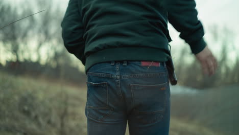 una vista cercana de un hombre con una chaqueta verde y vaqueros, visto desde atrás mientras se mueve con cautela a través de un entorno al aire libre