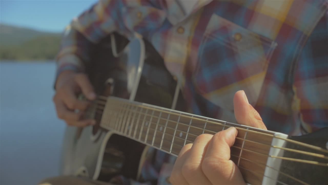близкий снимок молодого человека, играющего на акустической гитаре на берегу озера