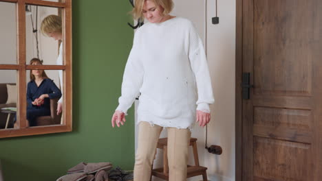 patient wears brown crocs by side of room near door, basket and coat rack in view, while mirror on green wall reflects therapist seated on sofa calmly waiting, creating professional atmosphere
