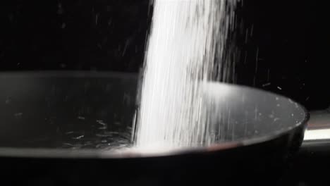 white refined sugar falling into a pan as part of a cooking recipe