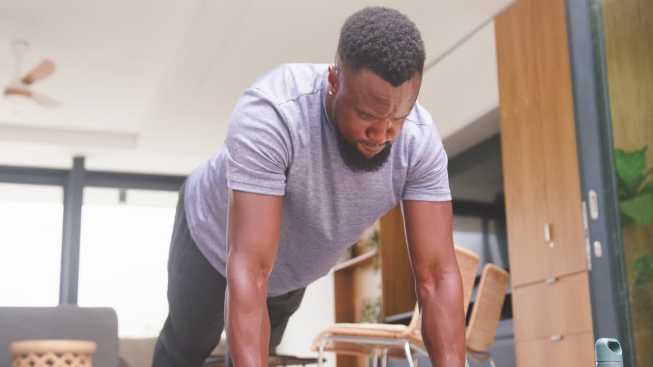 African American man in gray tee holding plank, alternating dumbbell rows on mat for core strength