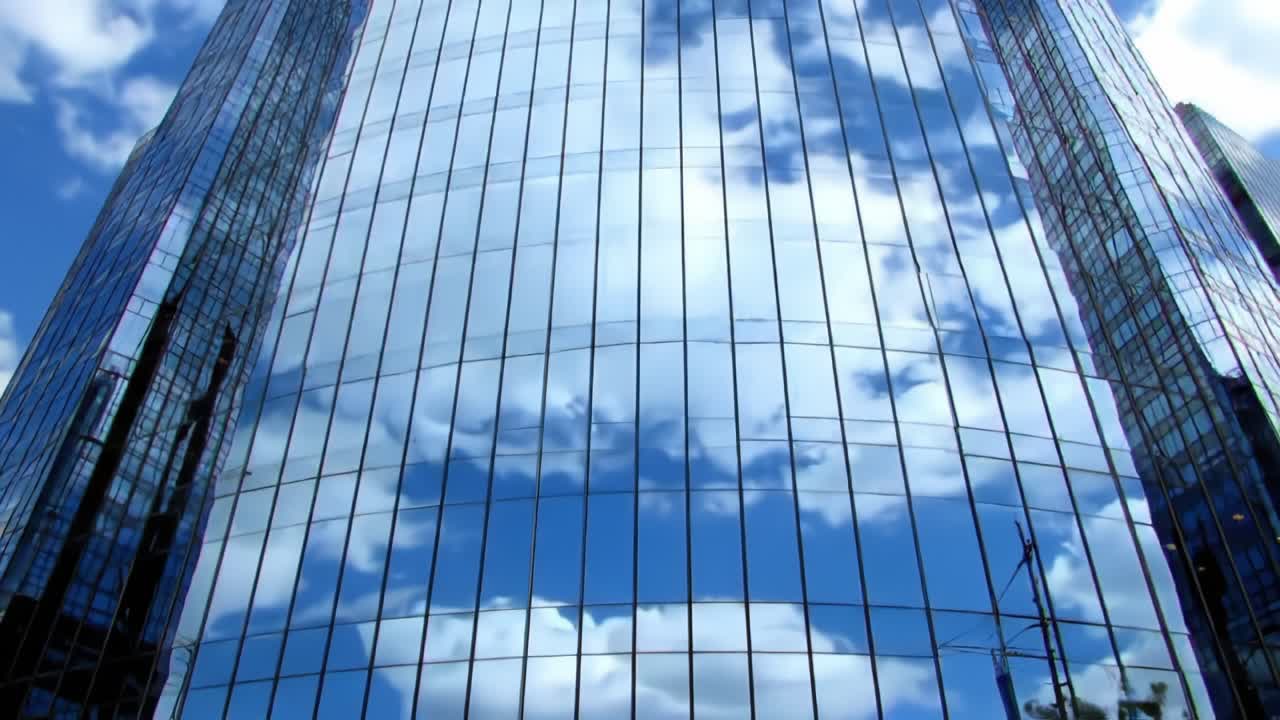 Reflections of Blue Skies and Clouds on a Modern Glass Building – A Stunning Visual Display of Urban Architecture Against a Bright Sky