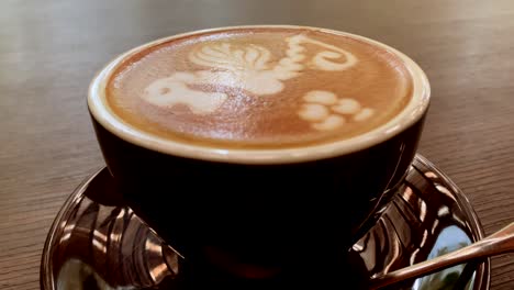 a cup of cafe latte with beautifully drawn horse art on the top was placed on the table with a teaspoon on the side