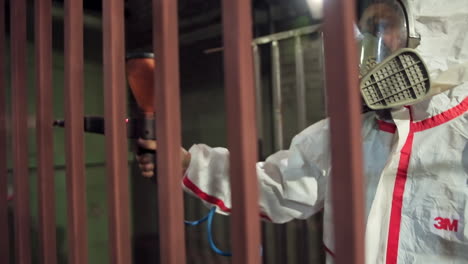 man in white protective suit and mask paints metal structure.worker in respirator using a spray gun to paint metal frame in a workshop. production facility.