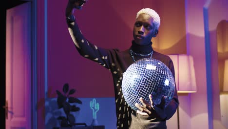 young stylish african american holding disco ball and making selfies using smartphone in a retro party at home