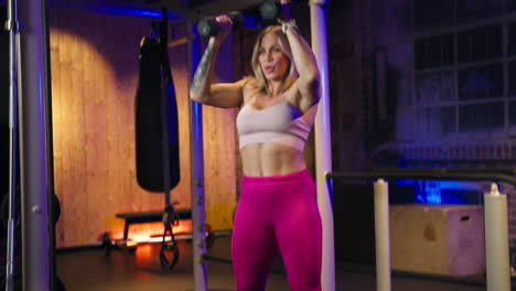 muscled woman combining squat and dumbbell shoulder press at the gym