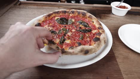 Cooked-marinara-pizza-on-a-plate-inside-Pizzeria-Bianco-in-Phoenix,-Arizona-with-a-hand-picking-up-a-slice-and-stable-video